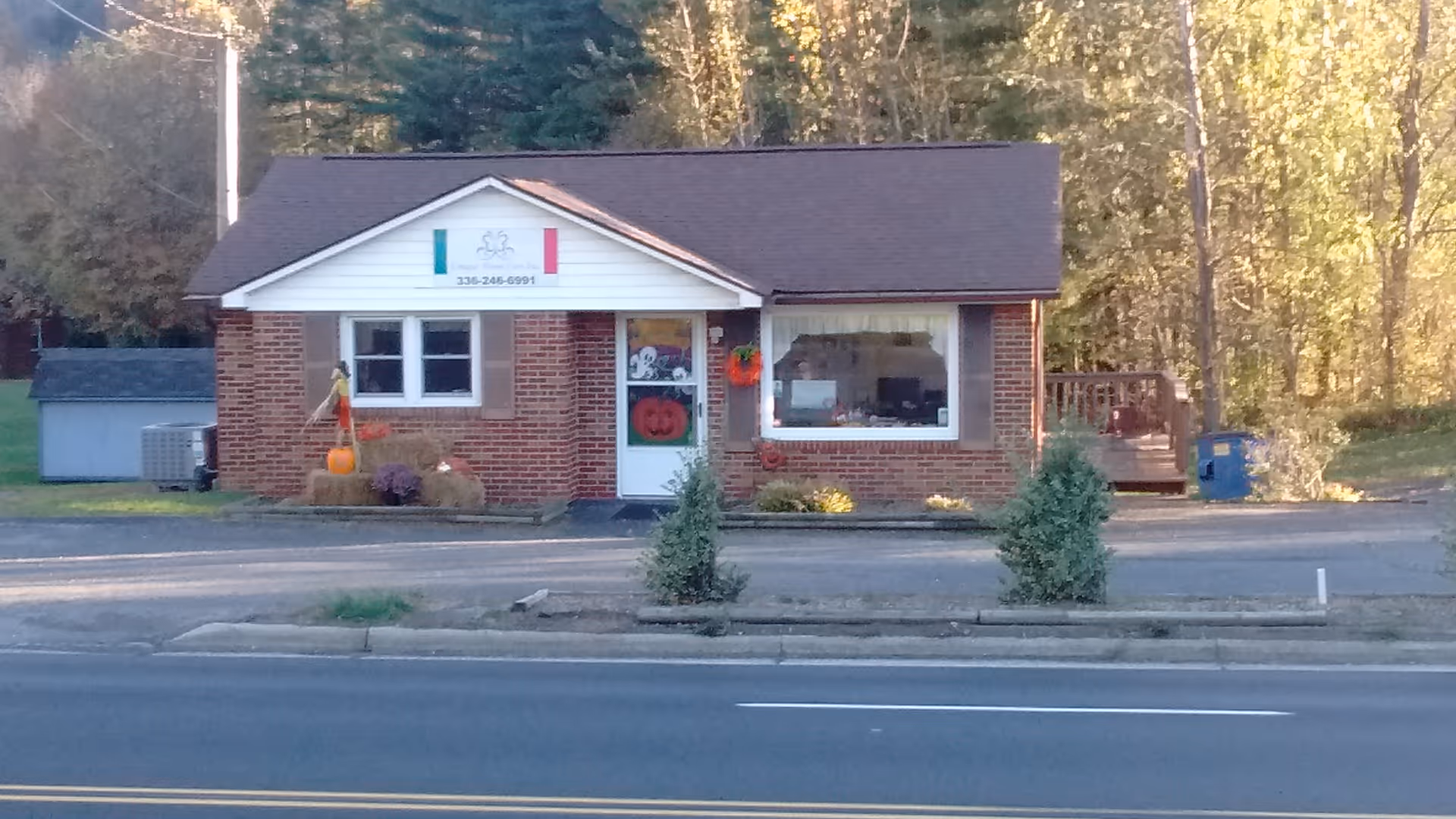 Small brick building with white trim and a front sign, Halloween decorations outside.