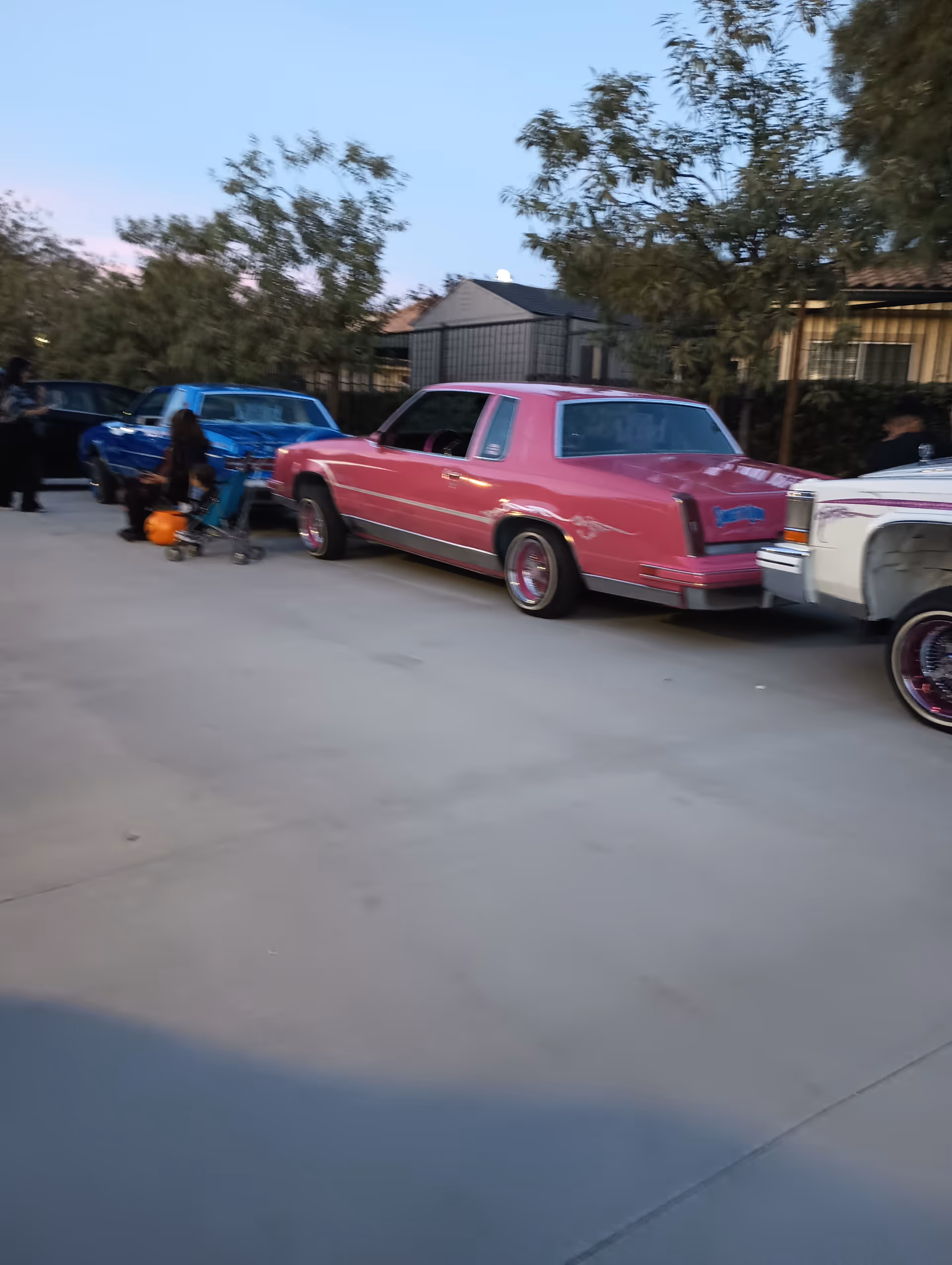 Outdoor parking area with colorful vintage cars and people gathered beside them.