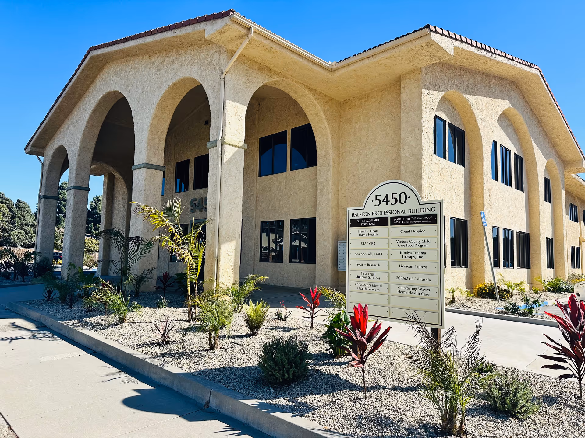 Sunlit beige building with arched entryways and a signboard amid desert landscaping