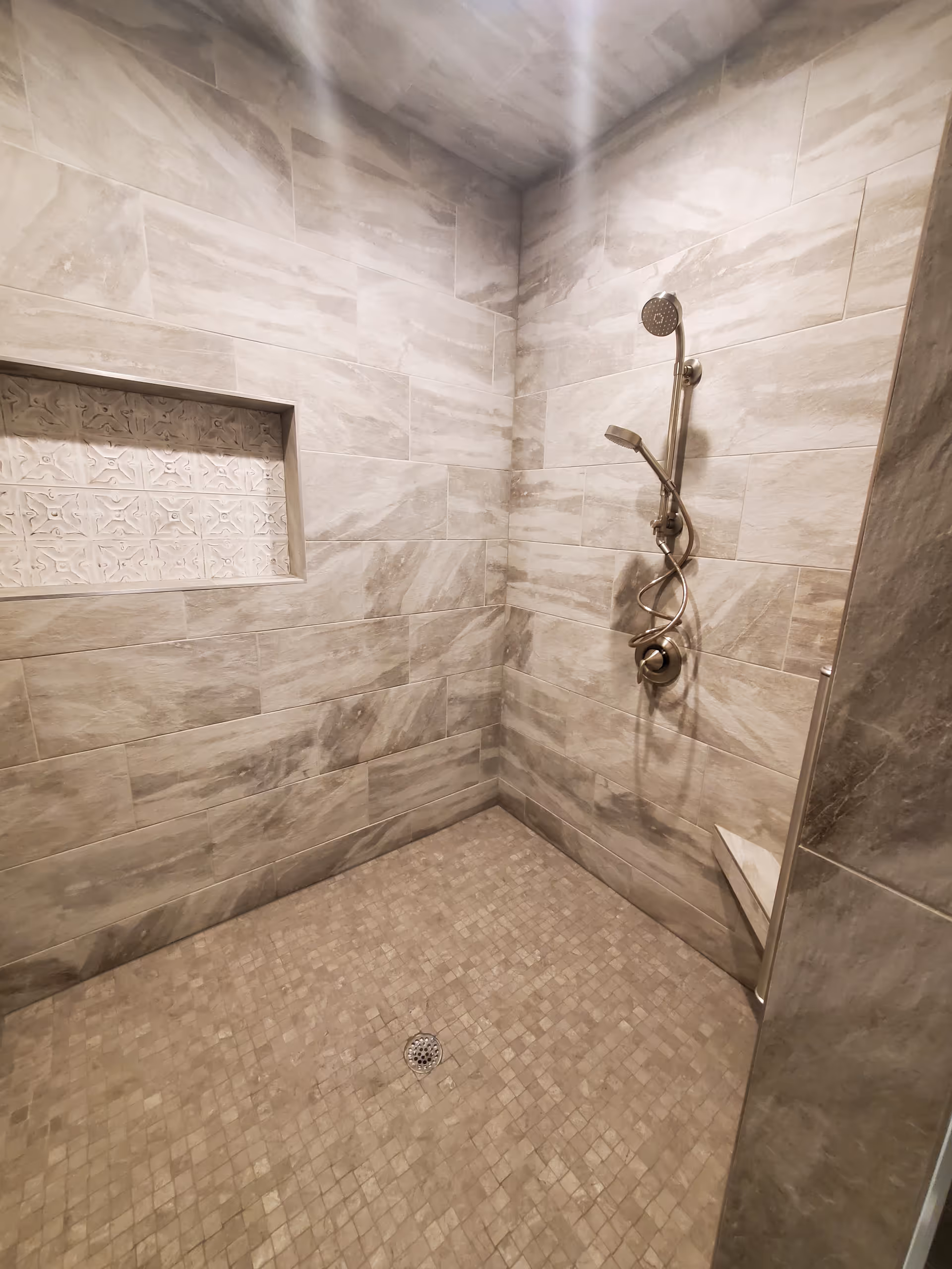 A tiled walk-in shower with handheld showerhead and built-in niche.
