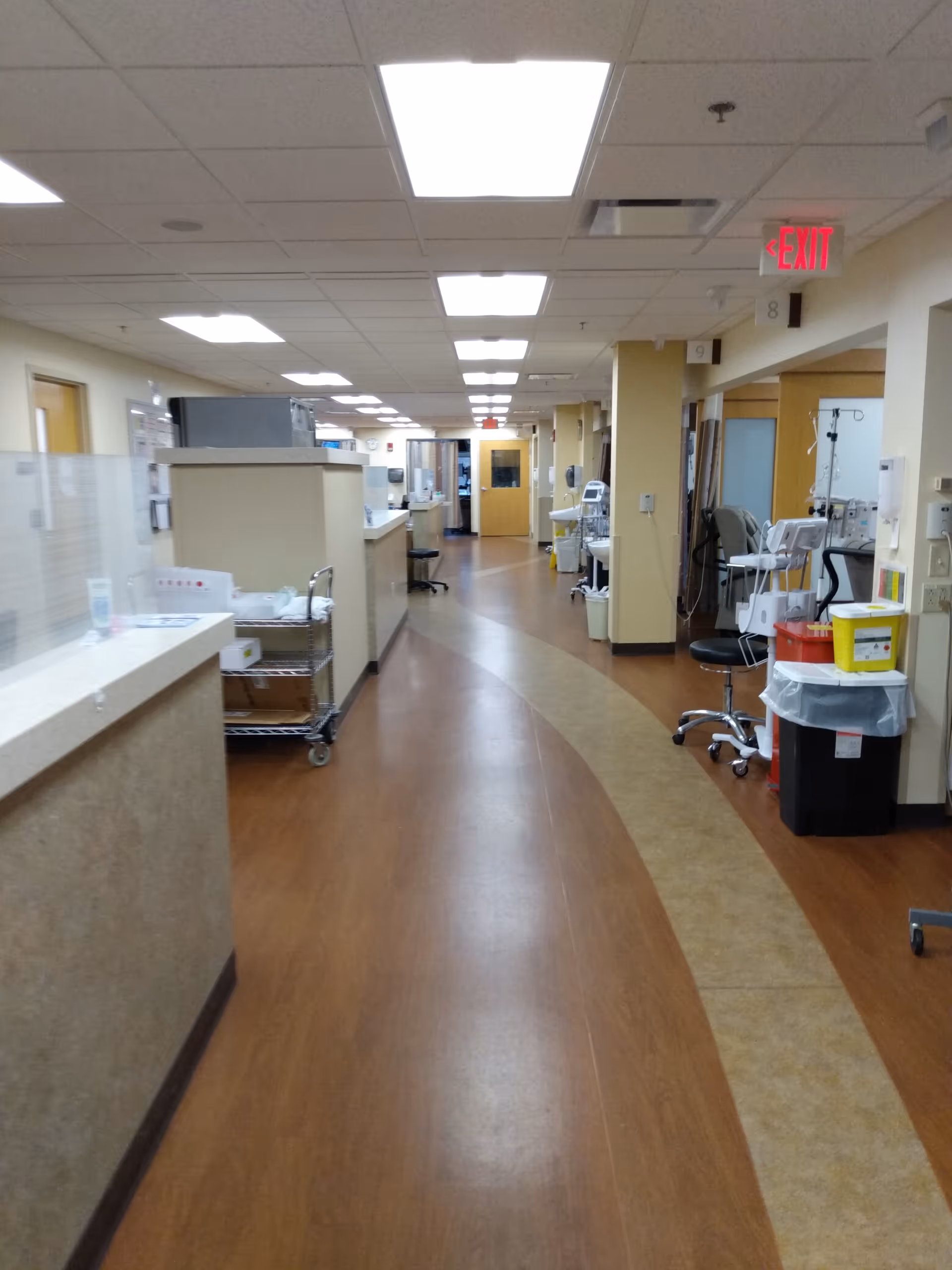 A long hospital corridor with medical equipment, carts, and bright ceiling lights.