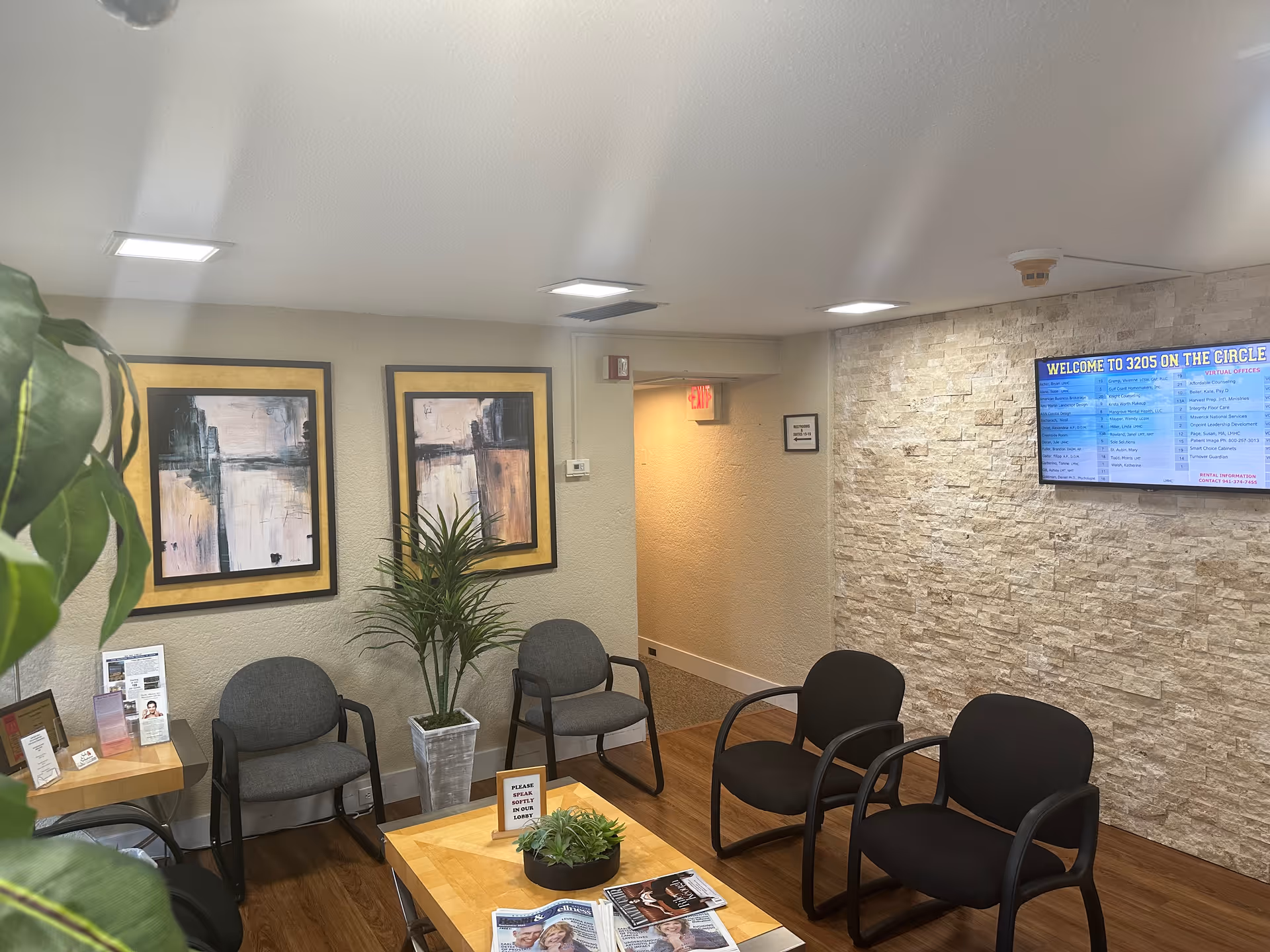 A calm waiting area in a facility with chairs, plants, framed art, and a wall-mounted schedule.