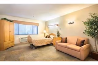 Assisted living apartment with bed, sofa, wardrobe, lamp, and a potted plant in a bright room.