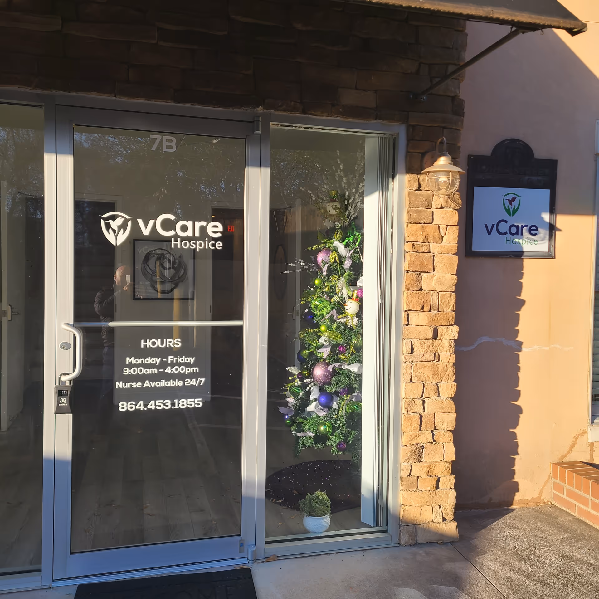 Exterior entrance of vCare Hospice with glass doors, stone facade, and wall sign.