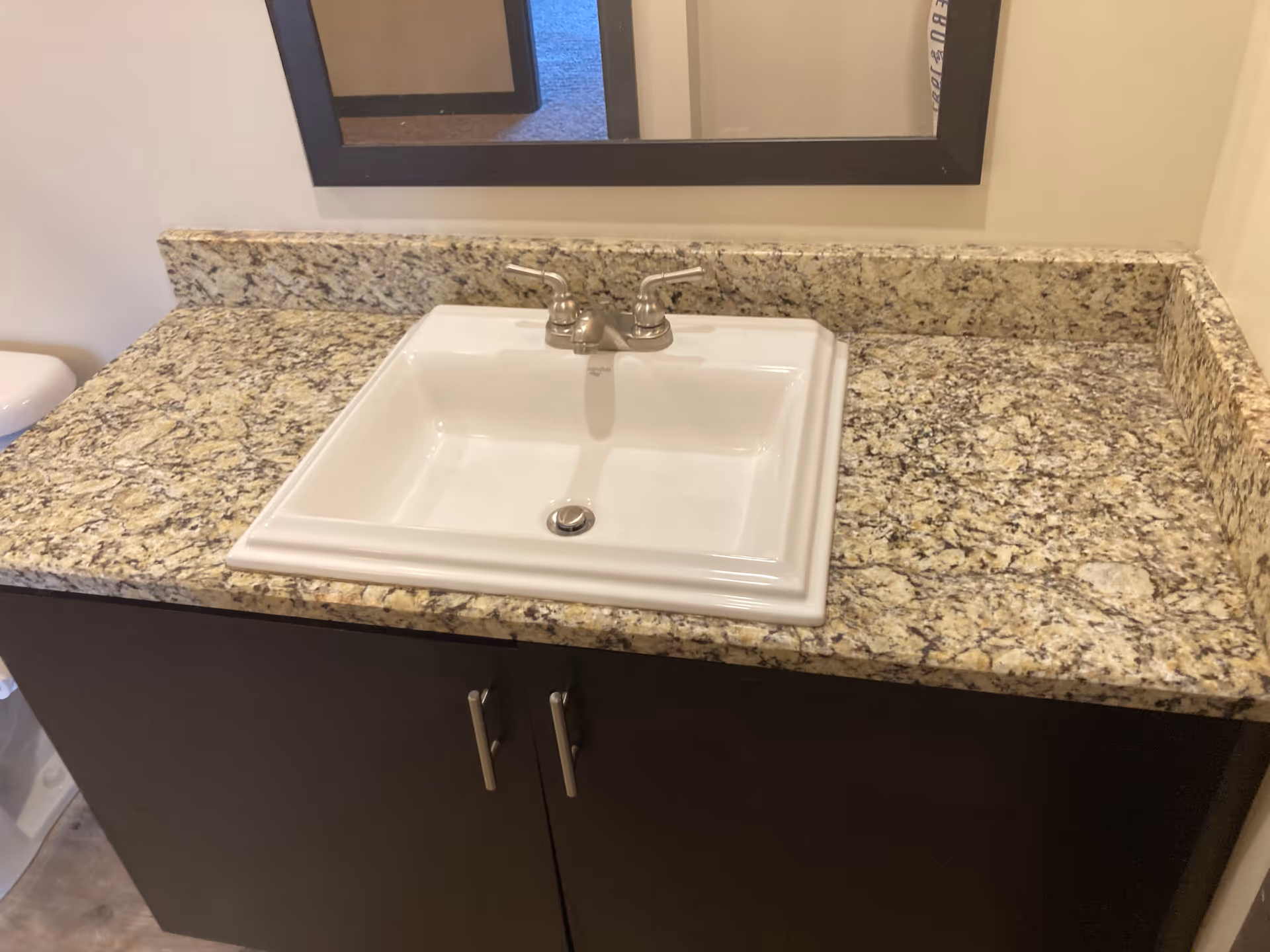 Granite countertop with white sink and mirror above a dark cabinet.