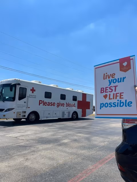 Blood donation bus and large sign in a parking lot outdoors.