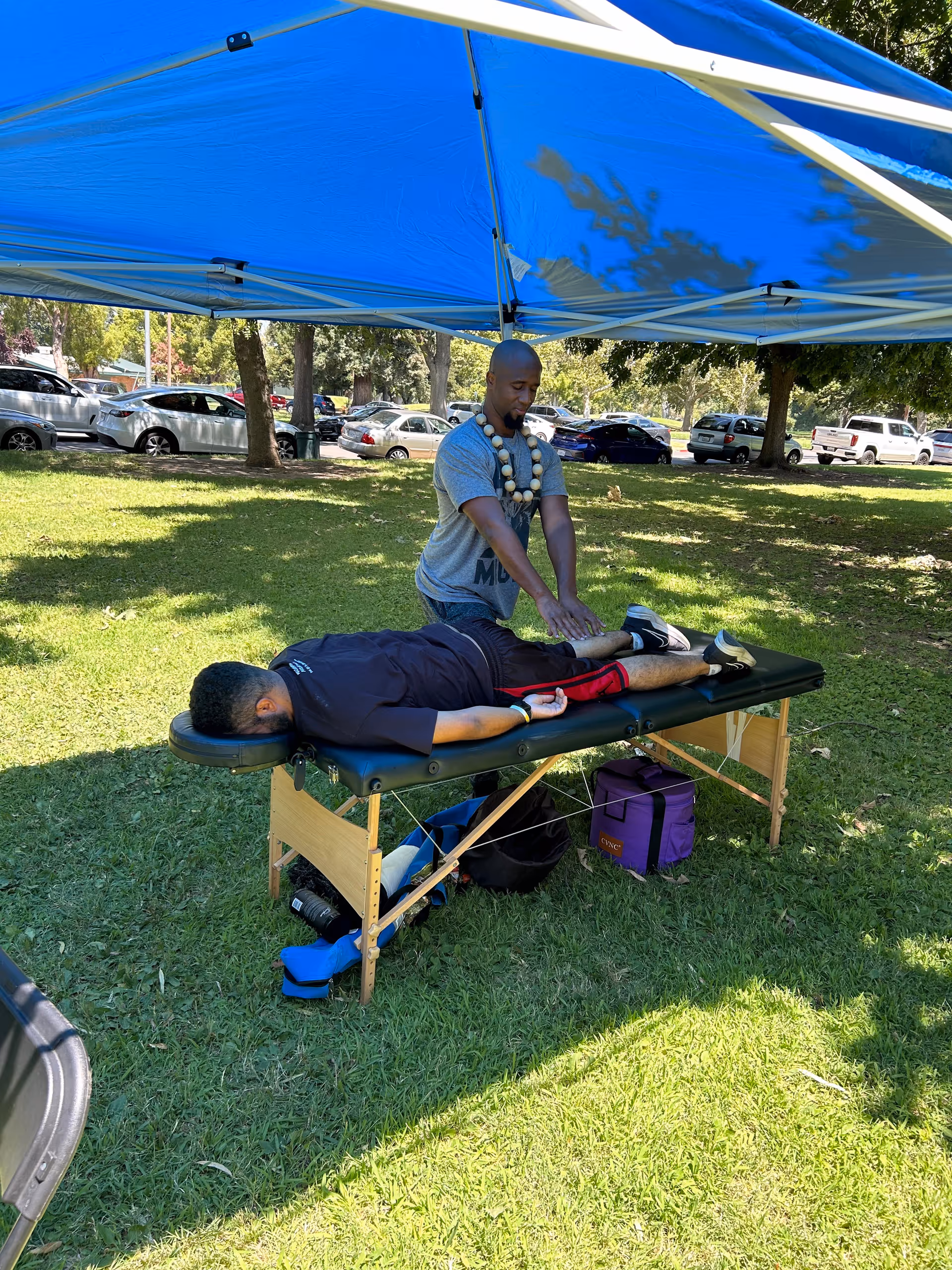 Therapist performs an outdoor massage on a portable table under a blue canopy.