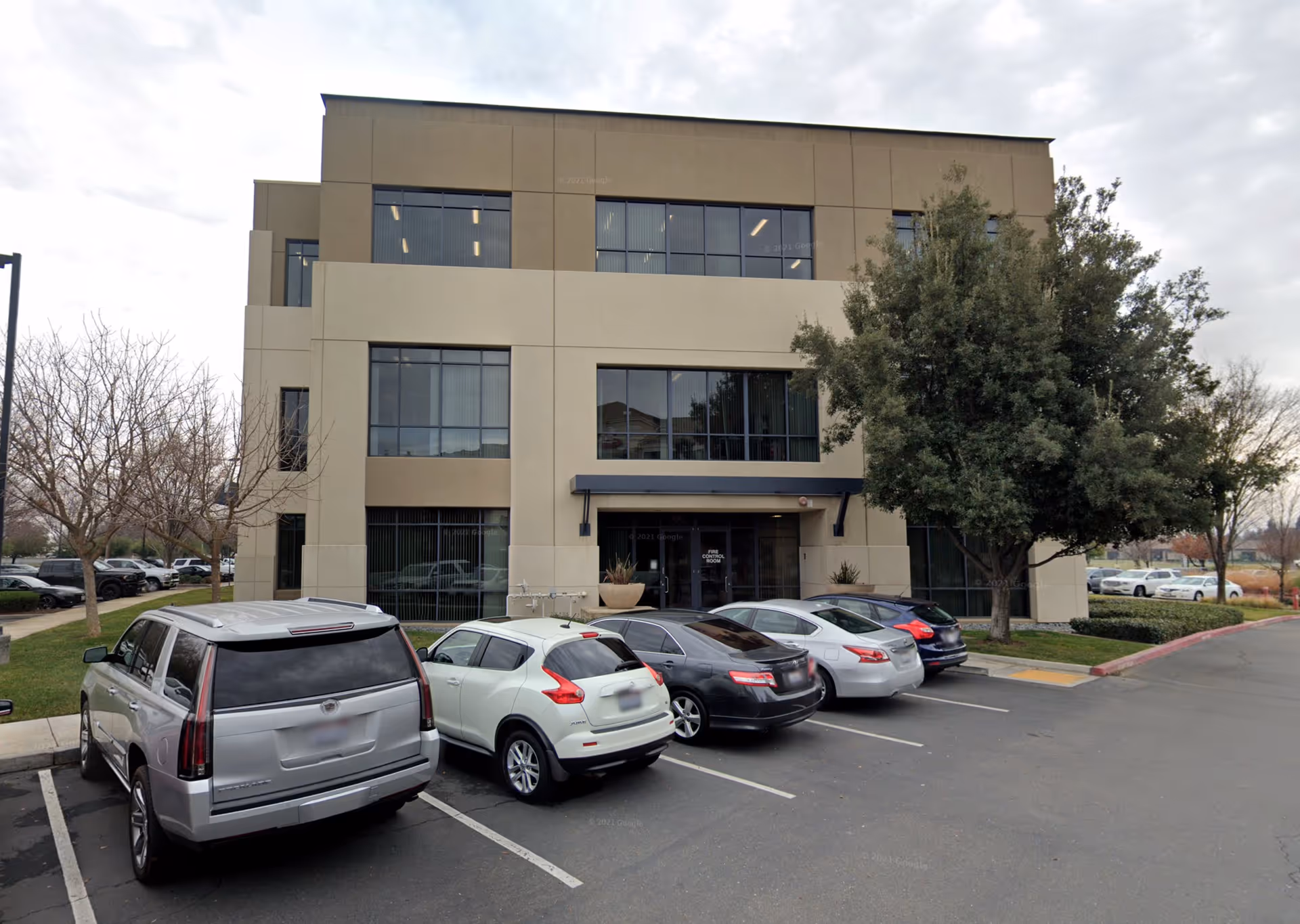 Modern multi-story office building with a row of parked cars in front