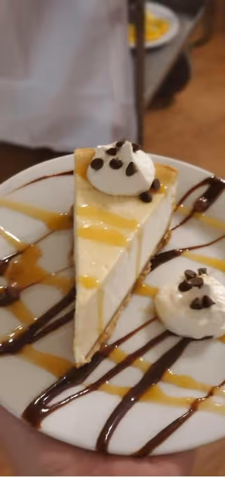 A slice of cheesecake on a plate drizzled with chocolate and caramel, topped with whipped cream and chocolate chips.