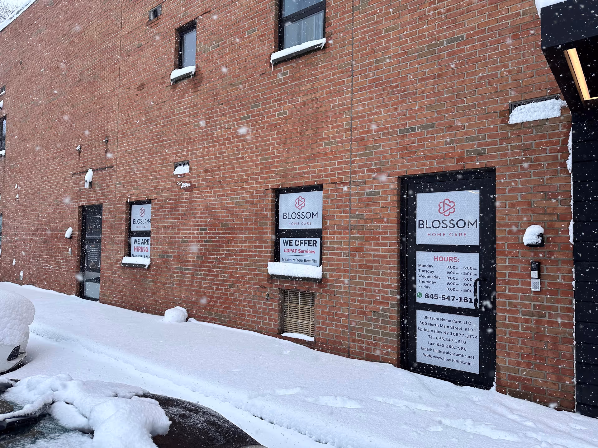 Brick exterior of Blossom Home Care building with snow, windows, and signs.