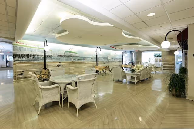 Spacious indoor lounge with wicker chairs, round tables, and a sea-themed mural along walls.