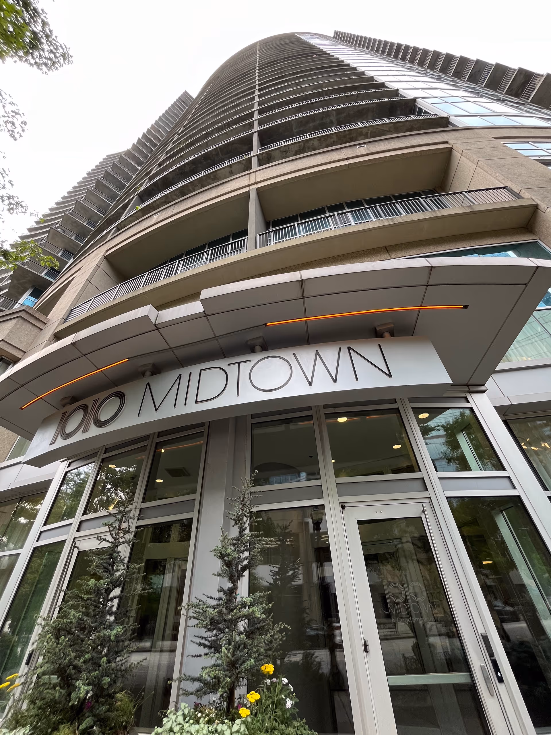 Low-angle view of a tall curved building entrance labeled 1010 Midtown with glass doors.