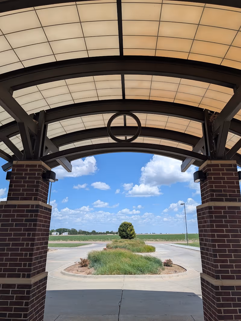 Brick entrance canopy with curved supports and circular ring overlooking a sunny landscape