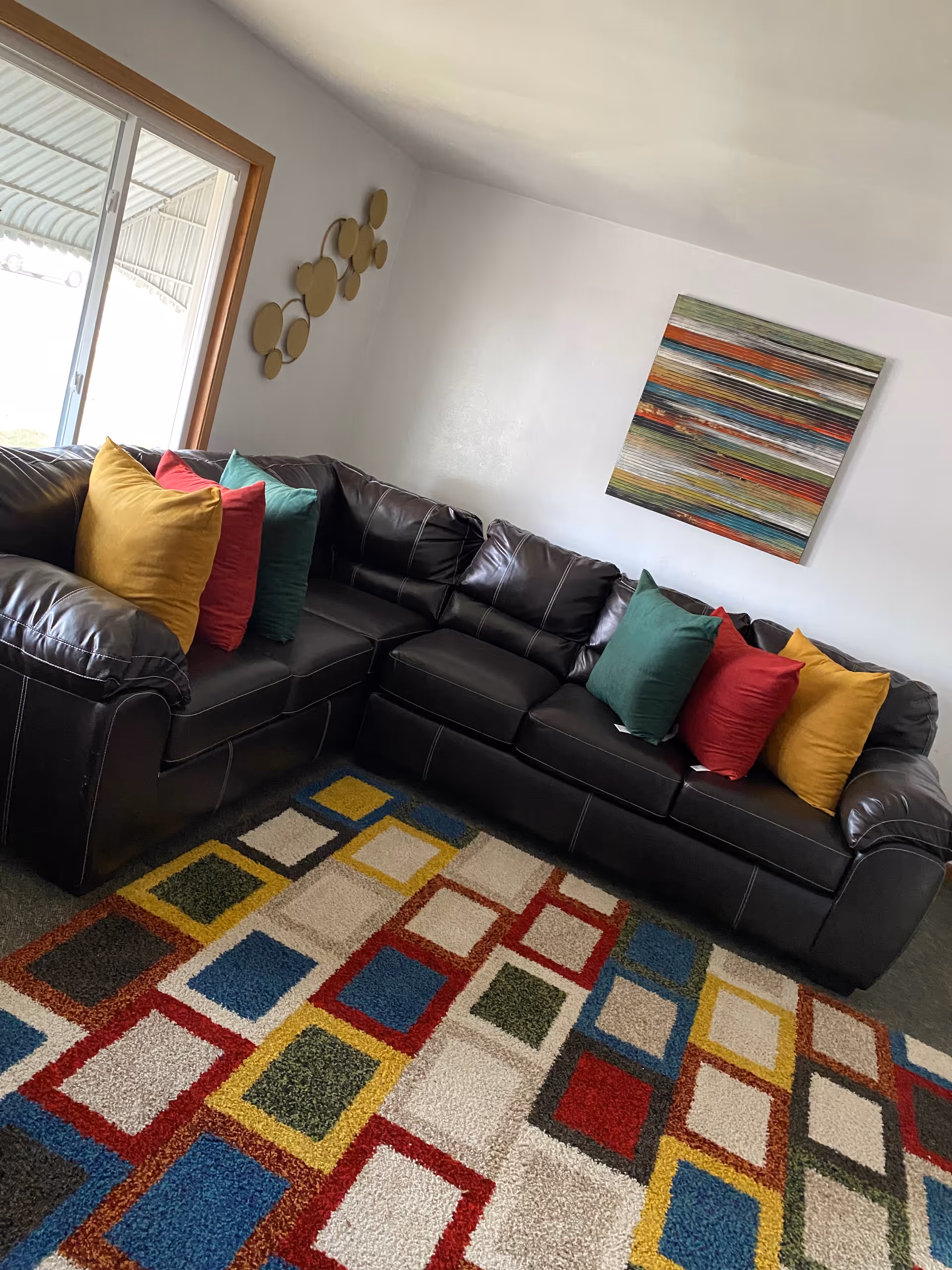 Black leather sectional sofa with colorful cushions and a vibrant patterned rug in a living room