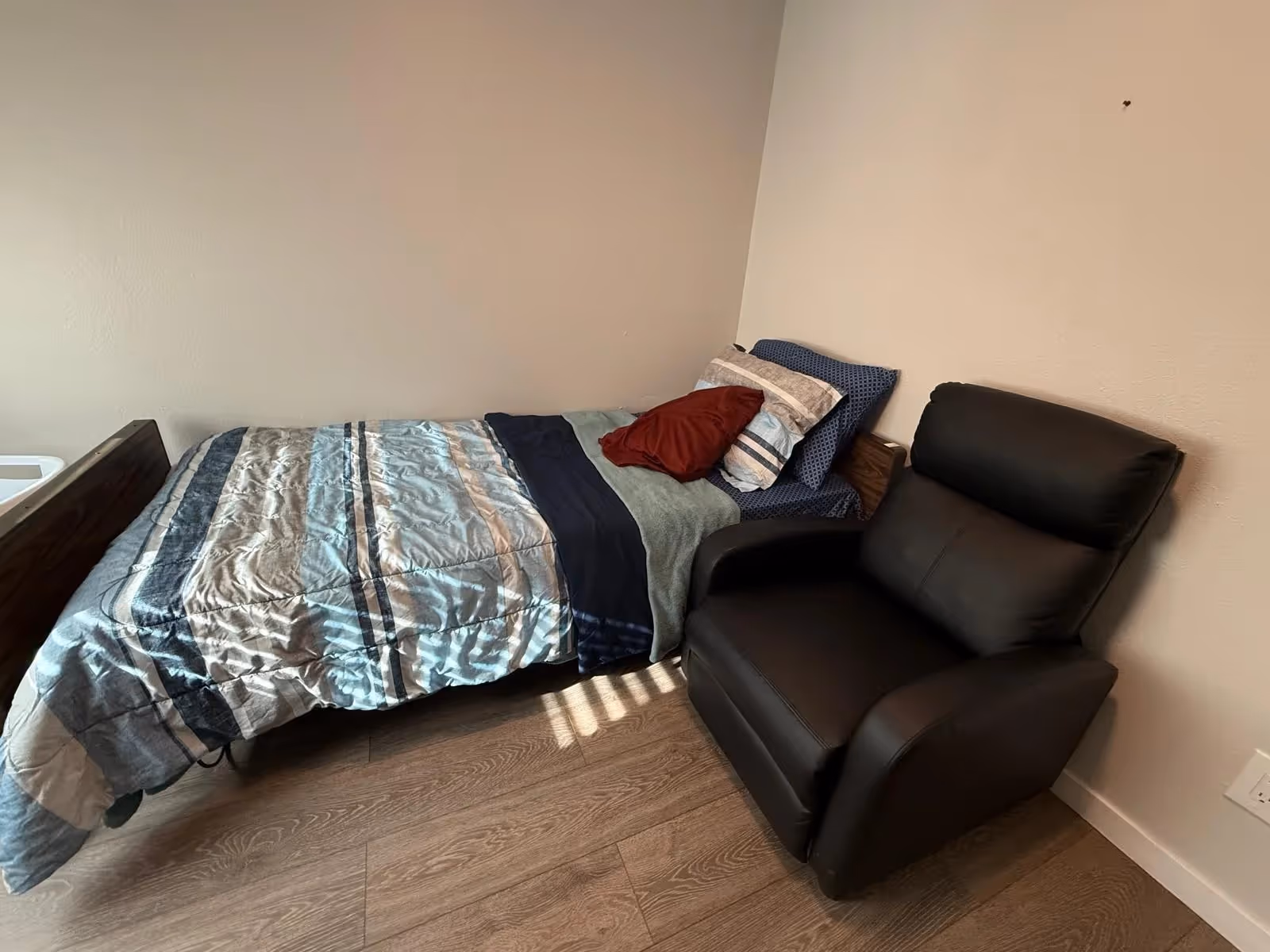 A small bedroom with a single bed, pillows, and a black recliner chair.