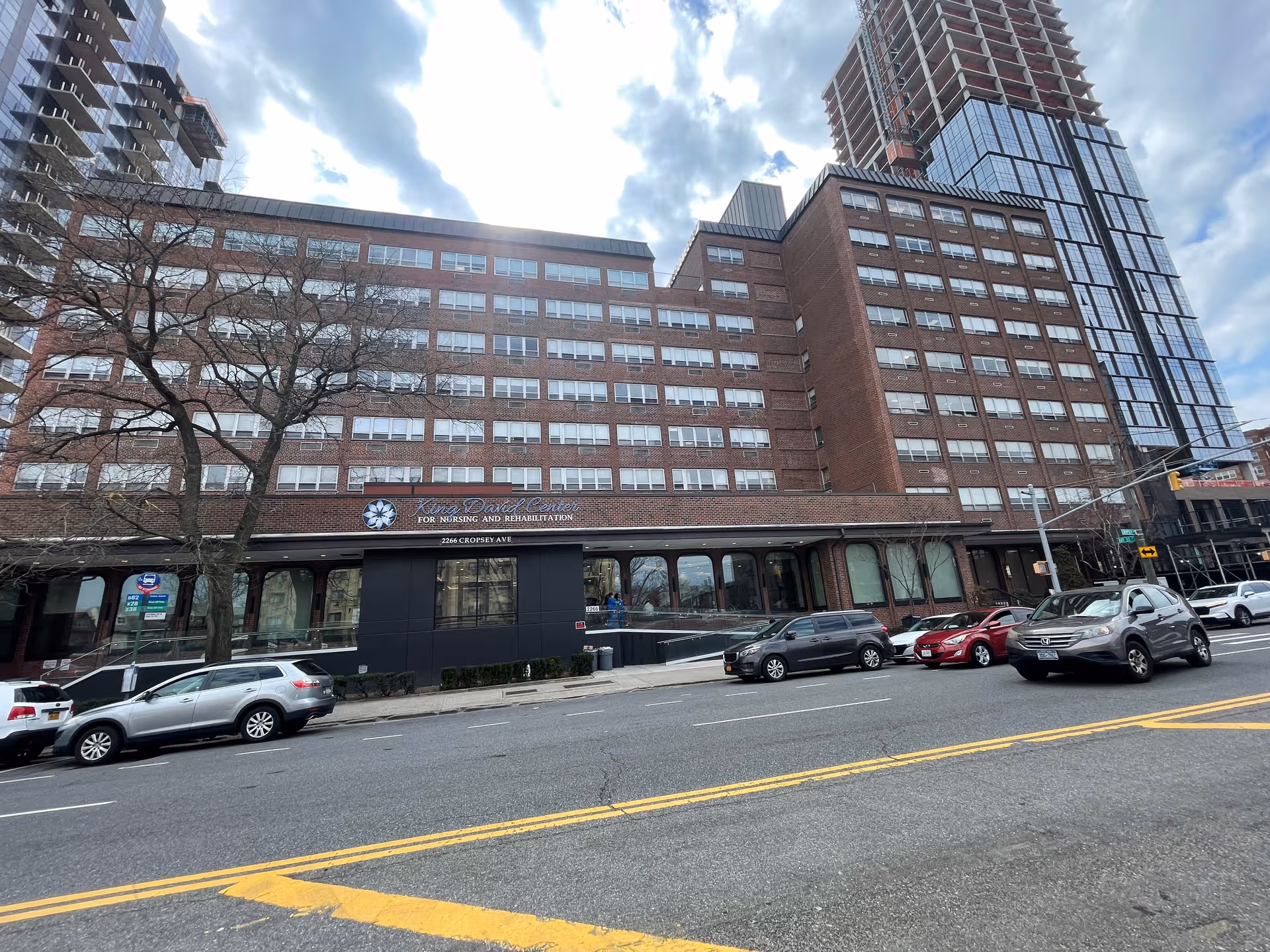 Large brick nursing facility with visible sign and many windows along a city street.