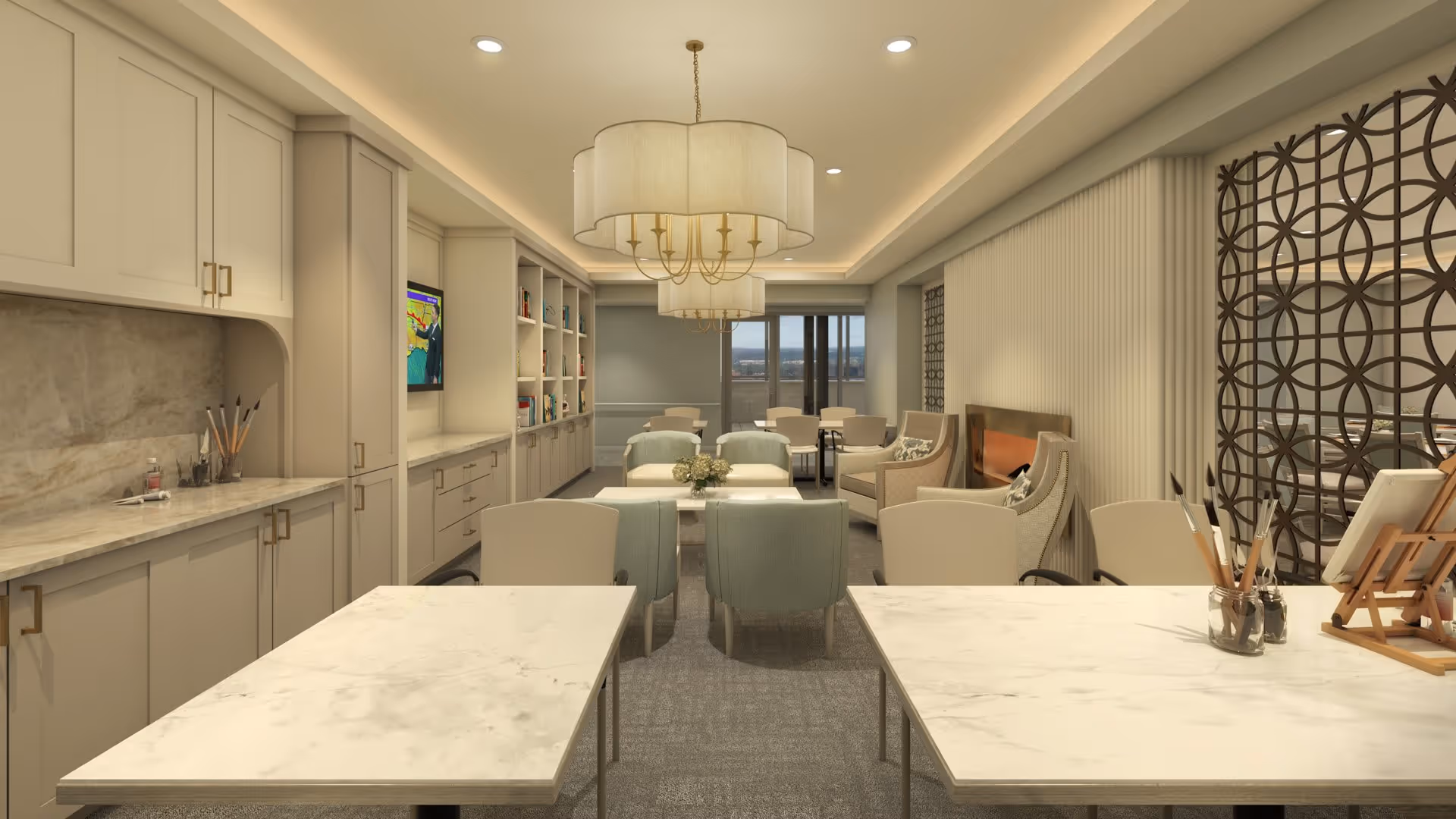 A well-lit, modern common area with two marble tables in the foreground, each holding paintbrushes and art supplies. The room features comfortable seating including armchairs and sofas arranged around a coffee table with a flower arrangement. Built-in cabinetry and shelves line the left wall, with a television mounted above. Decorative light fixtures hang from the ceiling, and a large window at the back provides a view outside. A decorative metal screen is visible on the right side of the room.