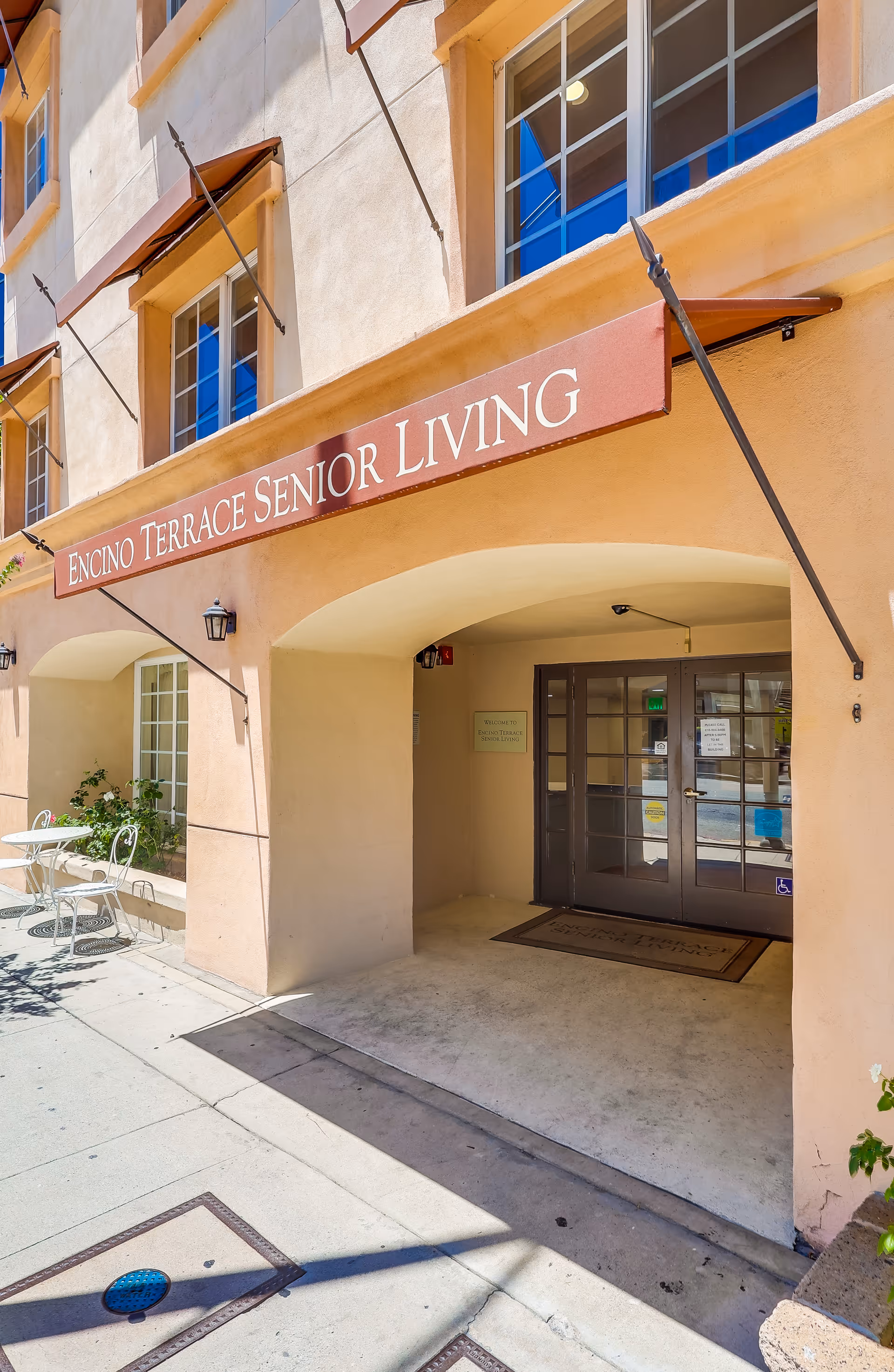 Entrance to Encino Terrace Senior Living building with sign and outdoor seating.