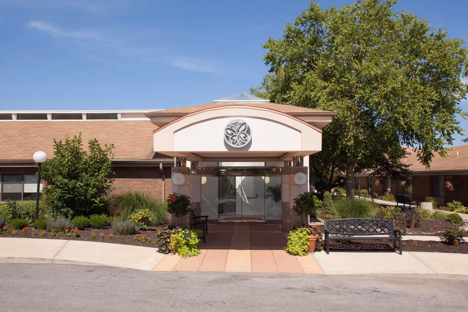 Front entrance of Delmar Gardens of Lenexa with landscaped surroundings and a bench.