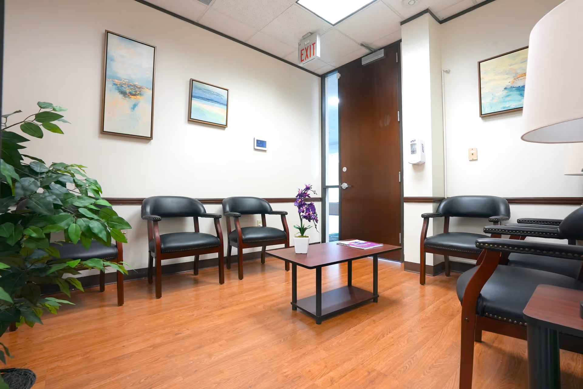 A quiet waiting area inside a medical facility with black chairs, a coffee table, and plants.