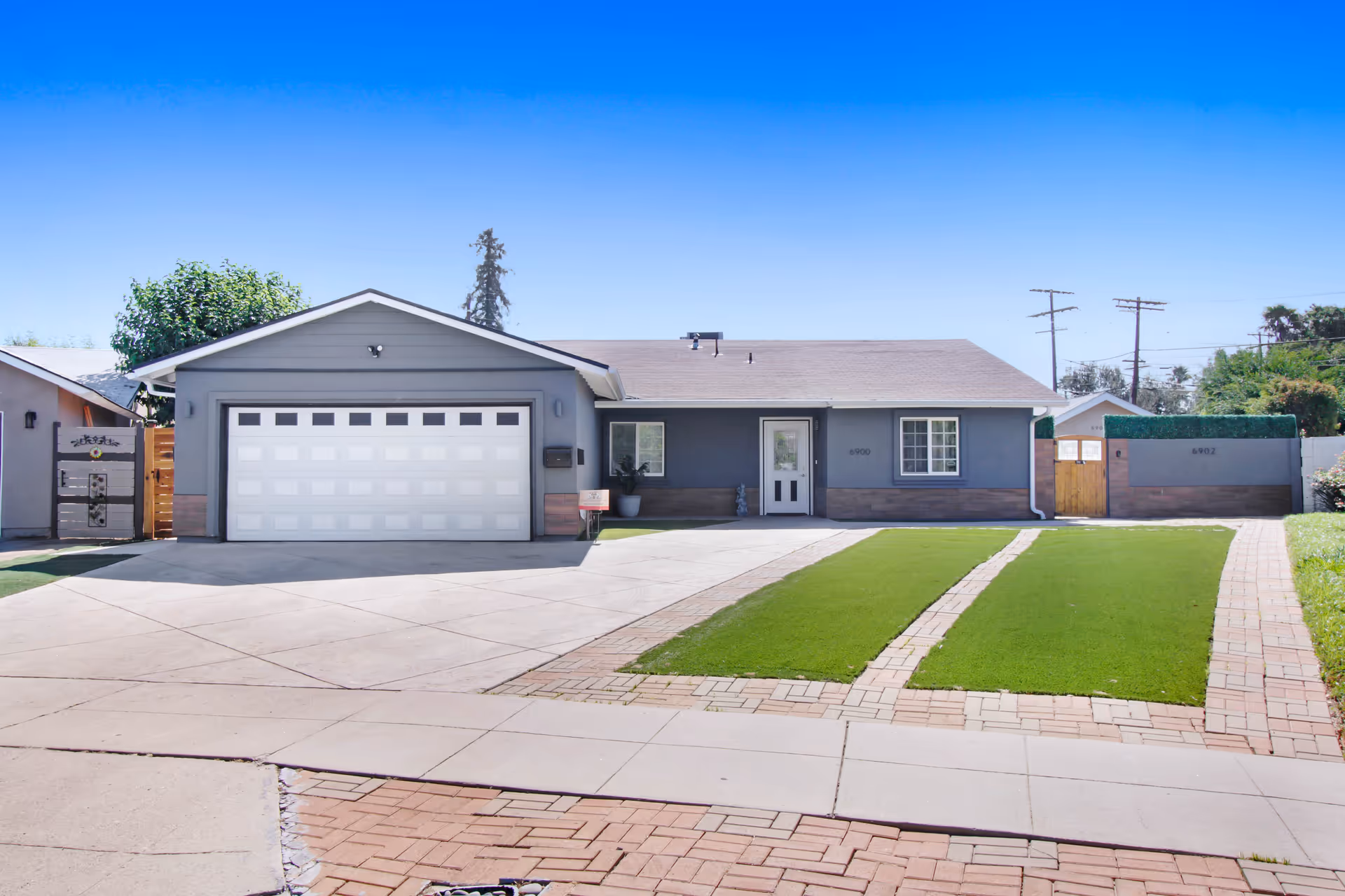 Single-story gray residence with an attached two-car garage, wide driveway, and two strips of manicured lawn leading to the front entrance.