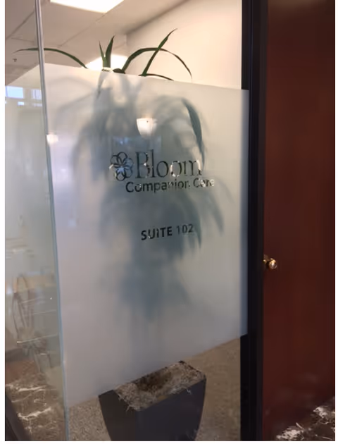Frosted glass door with Bloom Companion Care signage and a plant behind it.