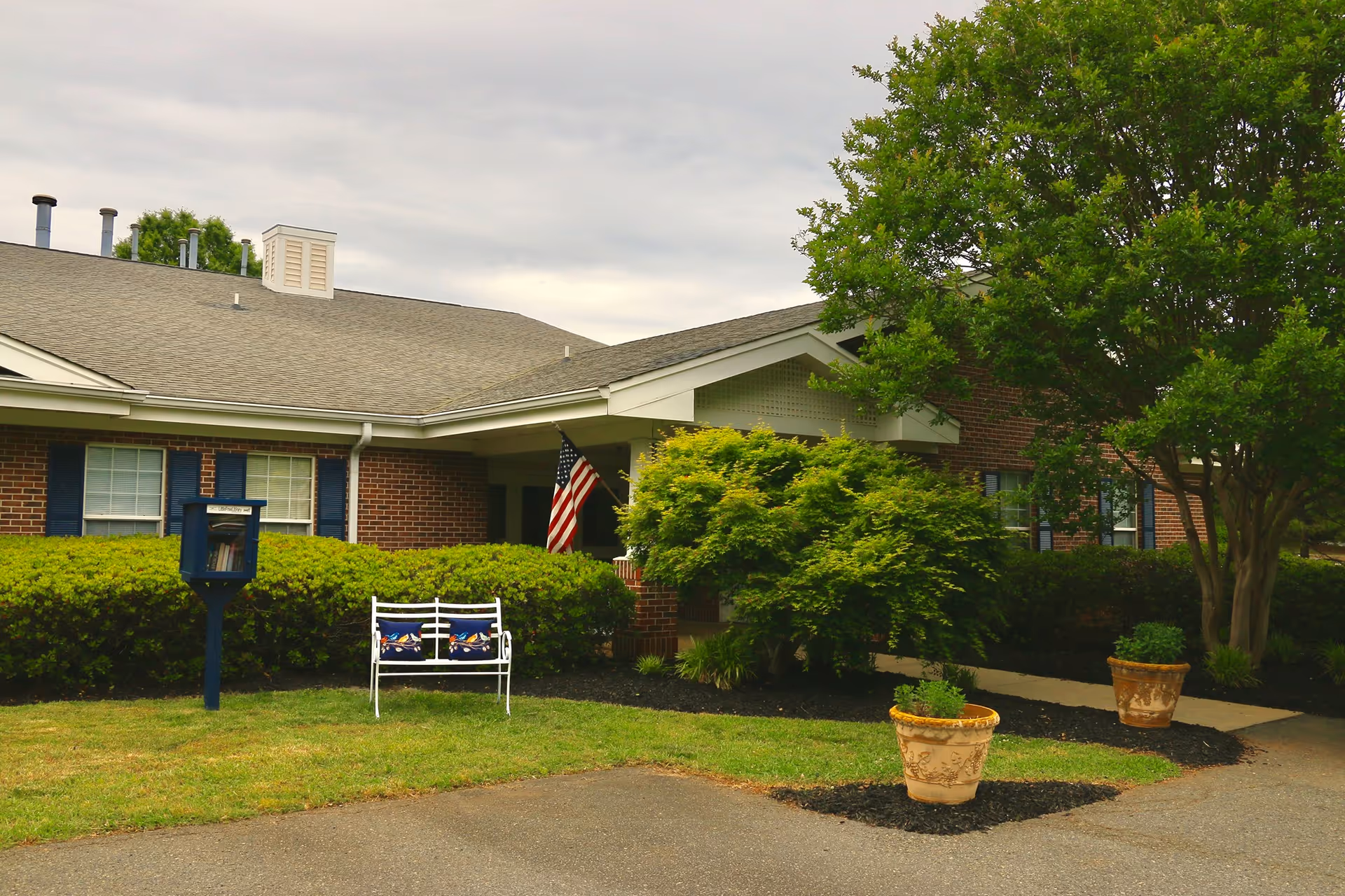 Exterior view of Preston House senior living facility with lawn, bench, and flag