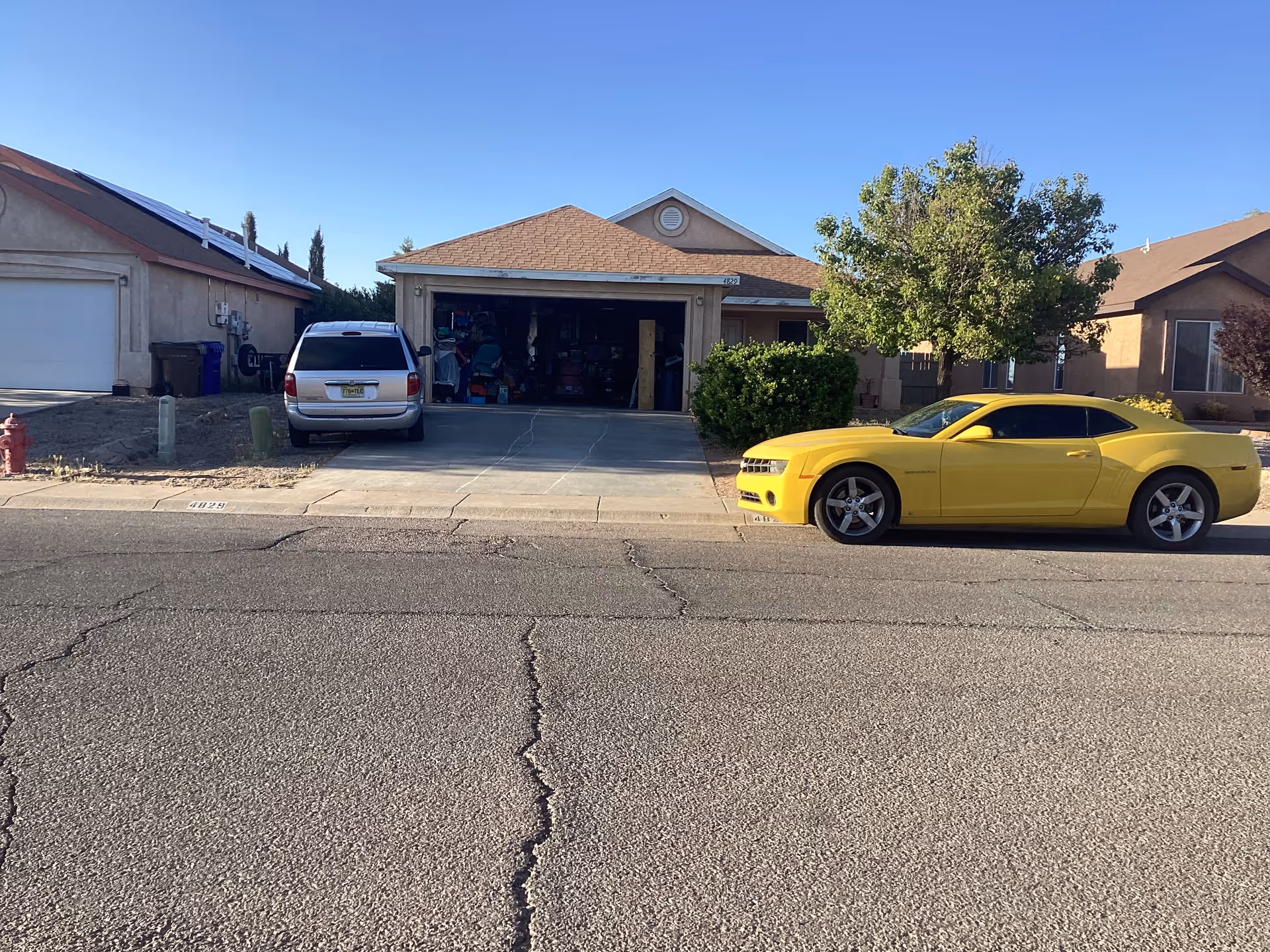 Residential street view with a yellow sports car parked on the curb and a garage open.