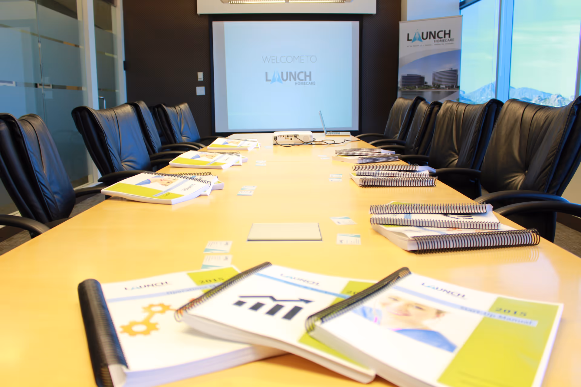 Empty conference room with a long table, notebooks, projector, and a welcome screen.