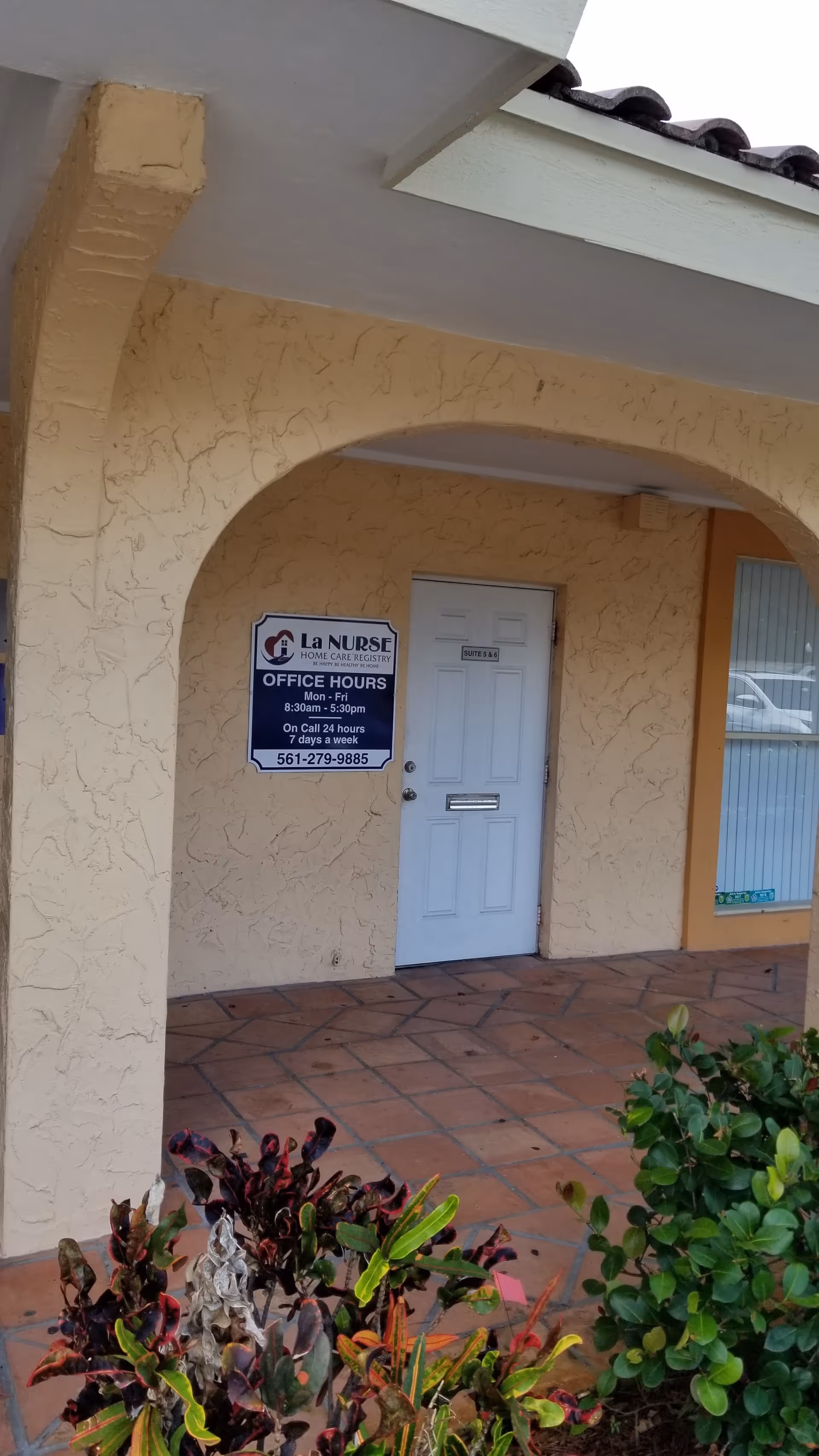 Beige stucco building entrance with arched porch and office sign reading La Nurse Home Care Registry.