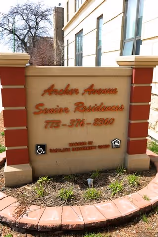 Exterior entrance sign reading Archer Avenue Senior Residences beside a beige building.
