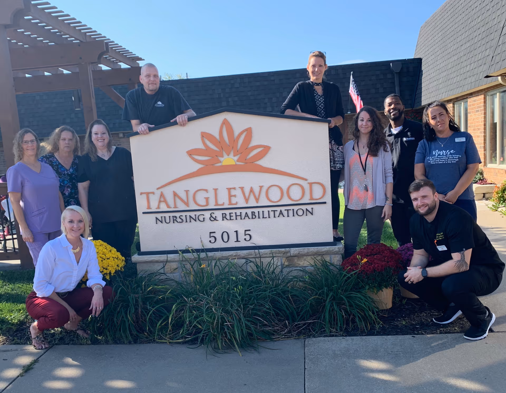 A group of staff members pose around a large Tanglewood Nursing & Rehabilitation sign outside the facility.