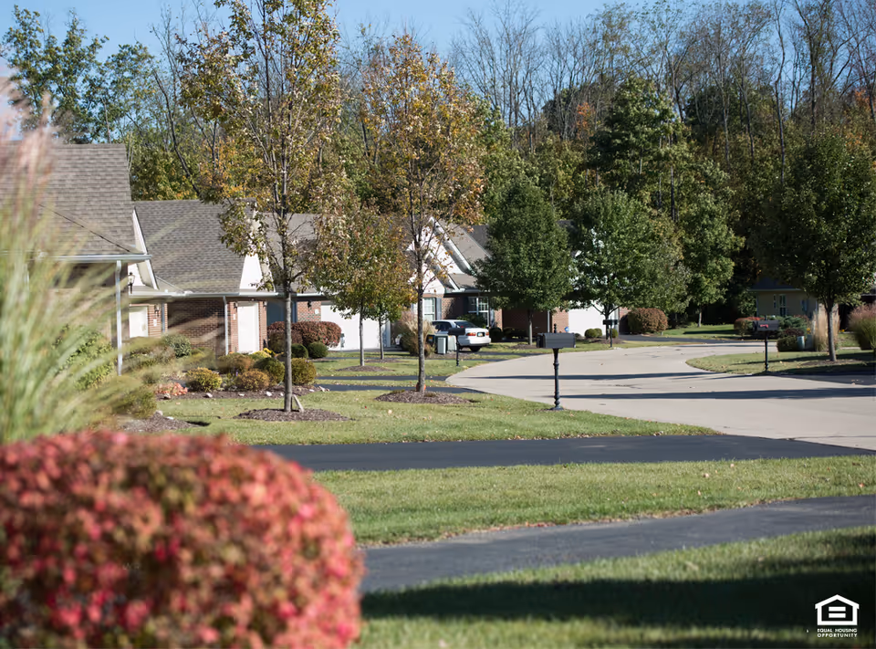 Curved street of senior living cottages with trees and manicured lawns.