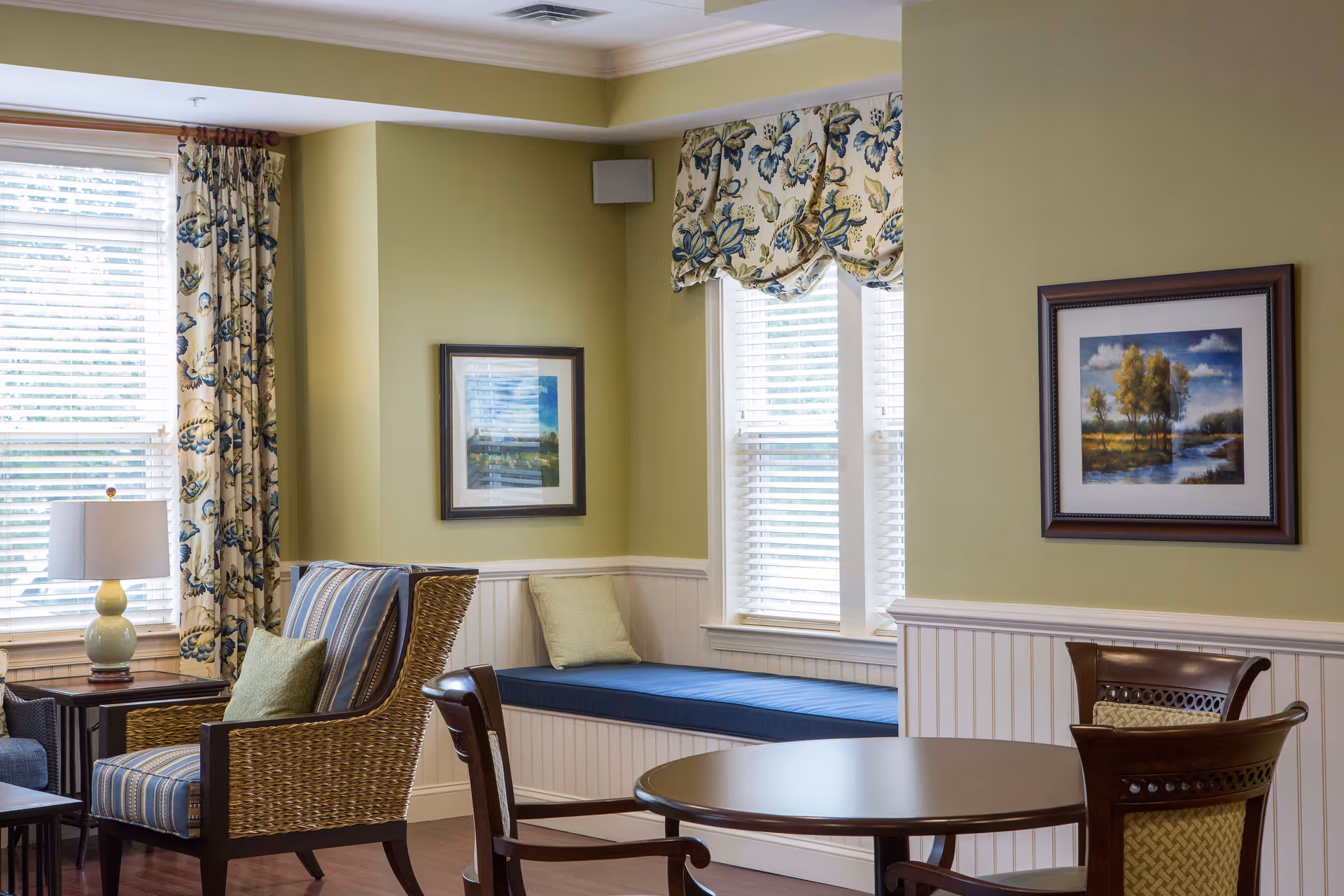 Bright living room lounge with seating, a round table, window seat, and framed landscape art.