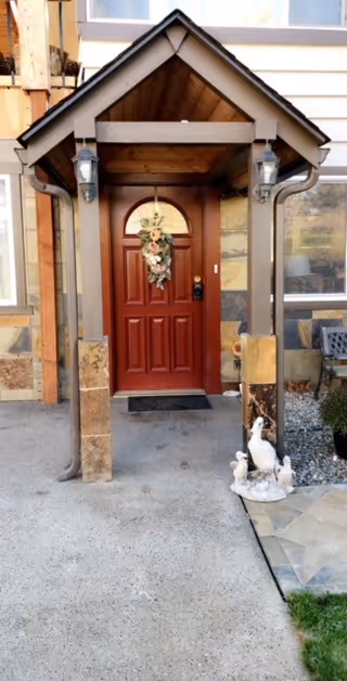 Red front door with wreath under a small porch, flanked by lamps.