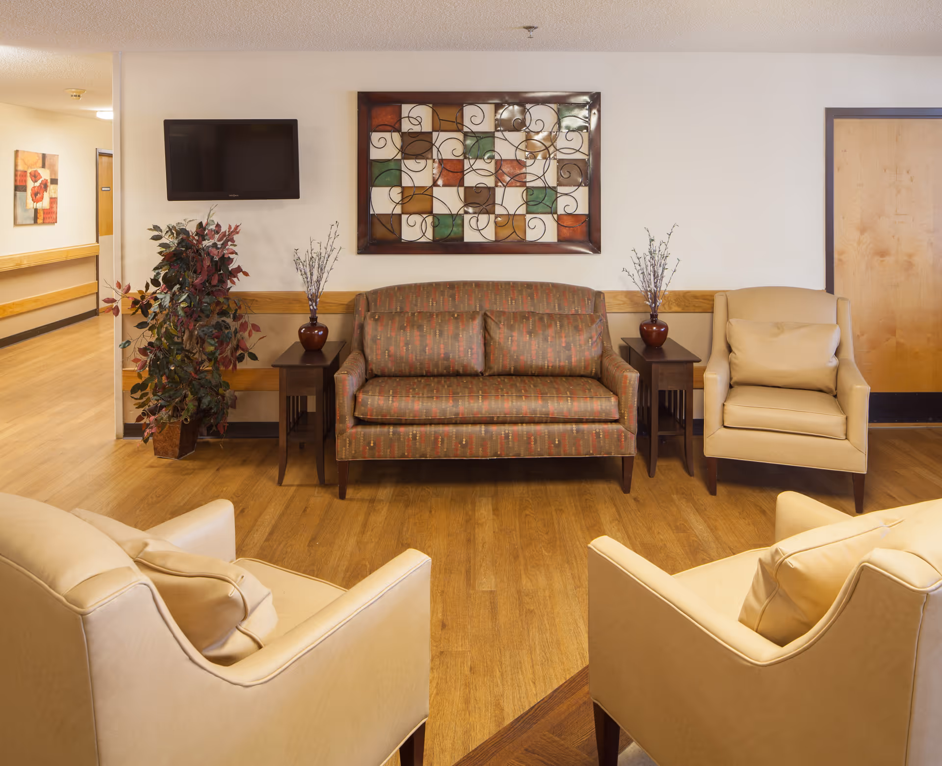 A cozy senior living lounge with sofa, chairs, wall art, and a TV.