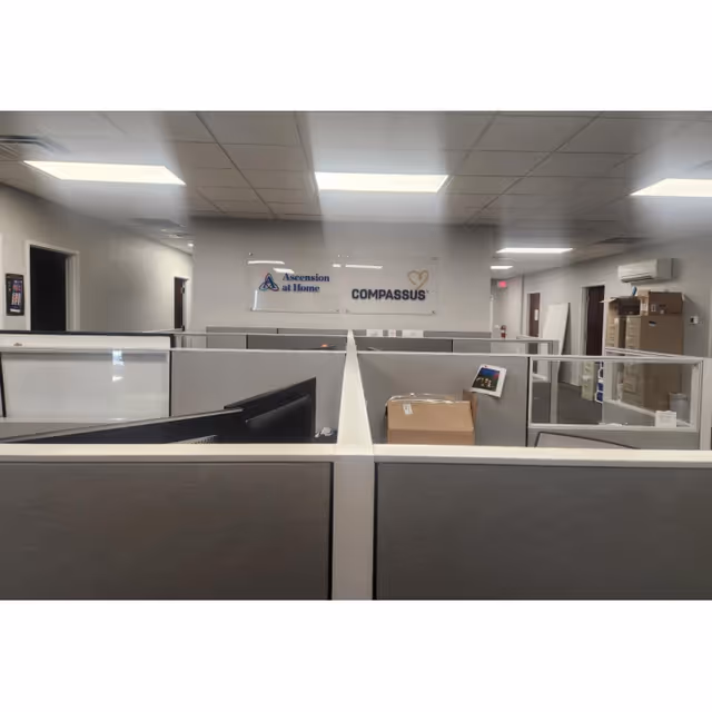 Open office cubicles inside Ascension at Home facility with wall sign.