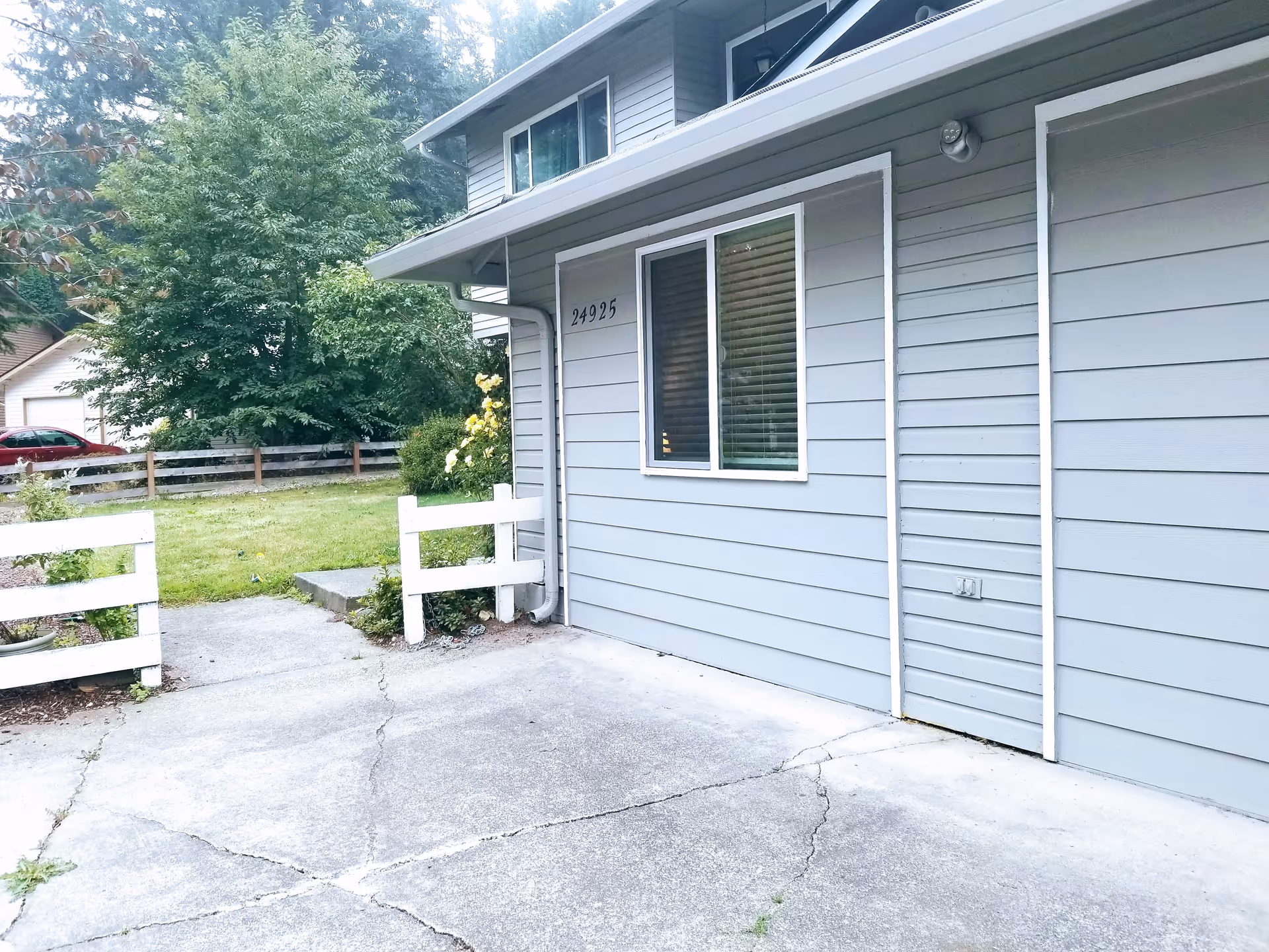 Gray single-story adult family home exterior with a driveway, window, and white fence.