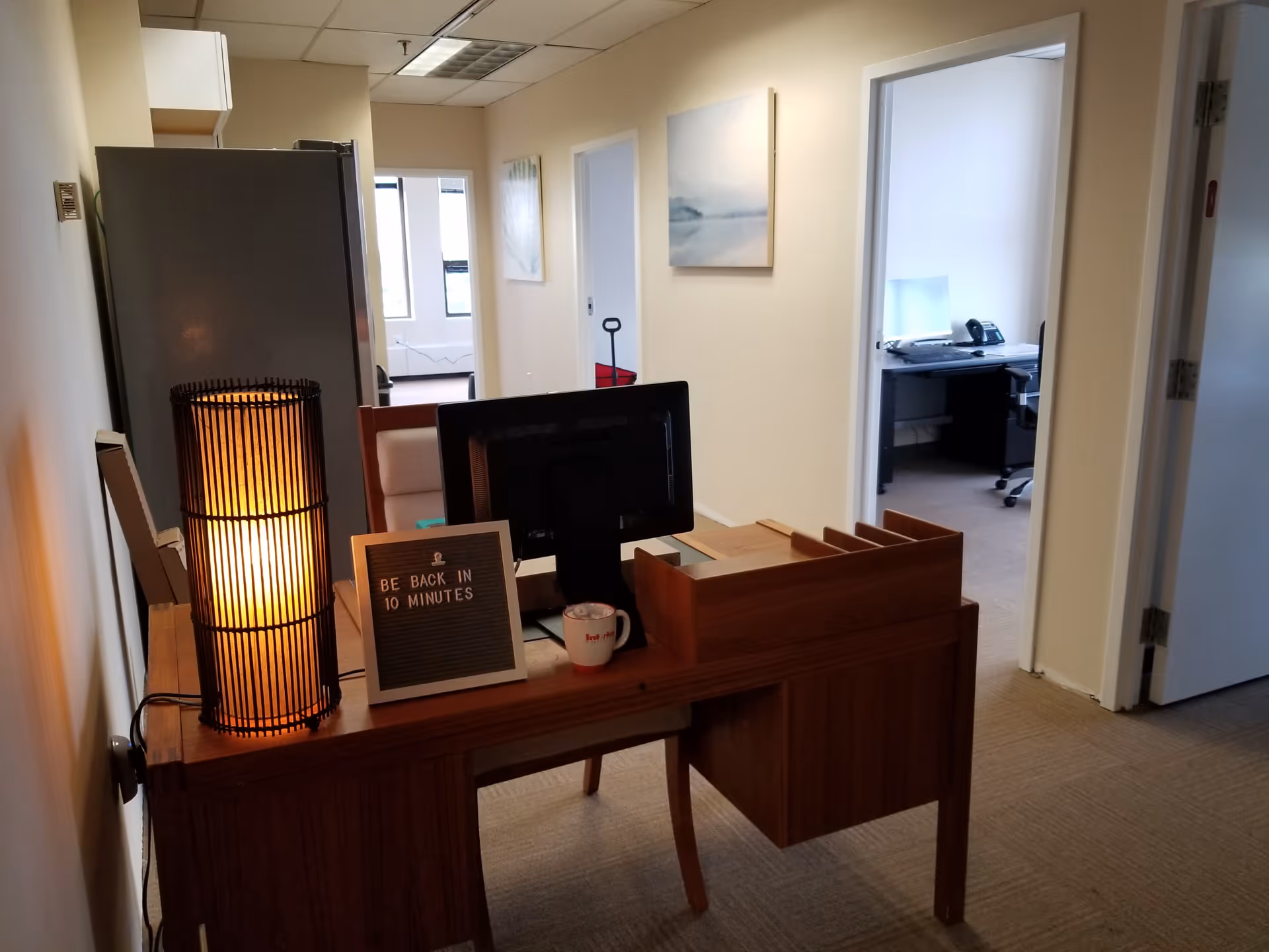 Reception desk with computer, lamp, and a sign in a hallway of a senior care facility.