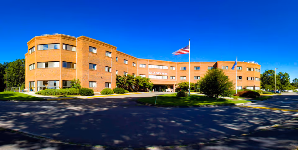 Brick senior living facility exterior with entrance, flags, and landscaping