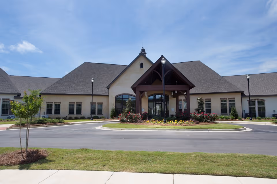 Front entrance of a senior living facility with a peaked wooden portico, circular driveway, and landscaped flower beds.