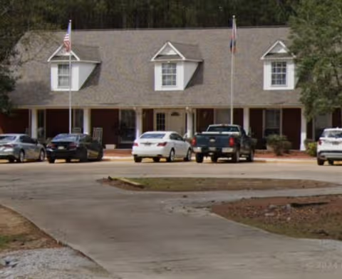 Front view of Oak Tree Manor Assisted Living Inc. building with parked cars and waving flags.