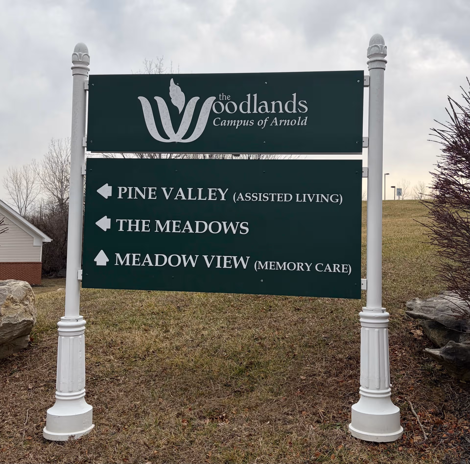 Large green exterior sign for Woodlands campus listing Pine Valley, The Meadows, Meadow View