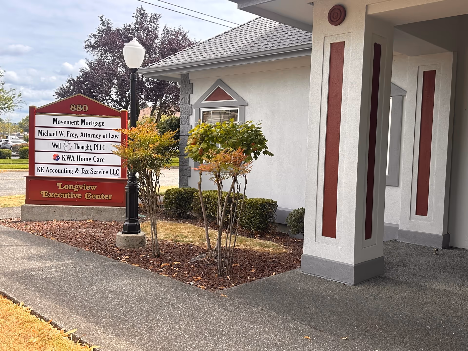 Exterior view of building entrance with a red sign and landscaped front yard.