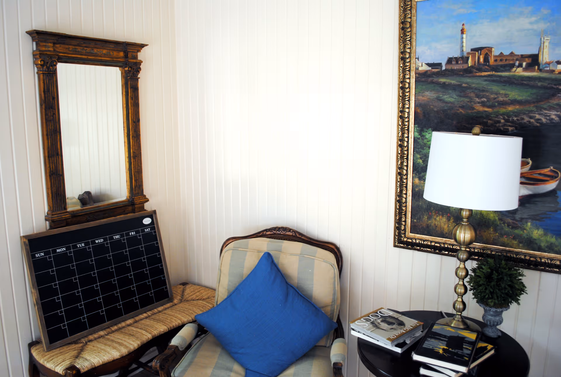 Cozy corner with striped chair, blue cushion, calendar board, ornate mirror, and table lamp.