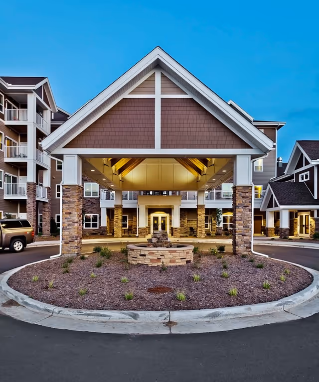 Covered porte-cochère entrance with a circular landscaped island and fountain in front of a multi-story senior living building.