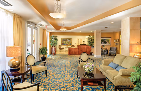 Bright lobby seating area with sofas, chairs, tables, plants, and a reception desk.