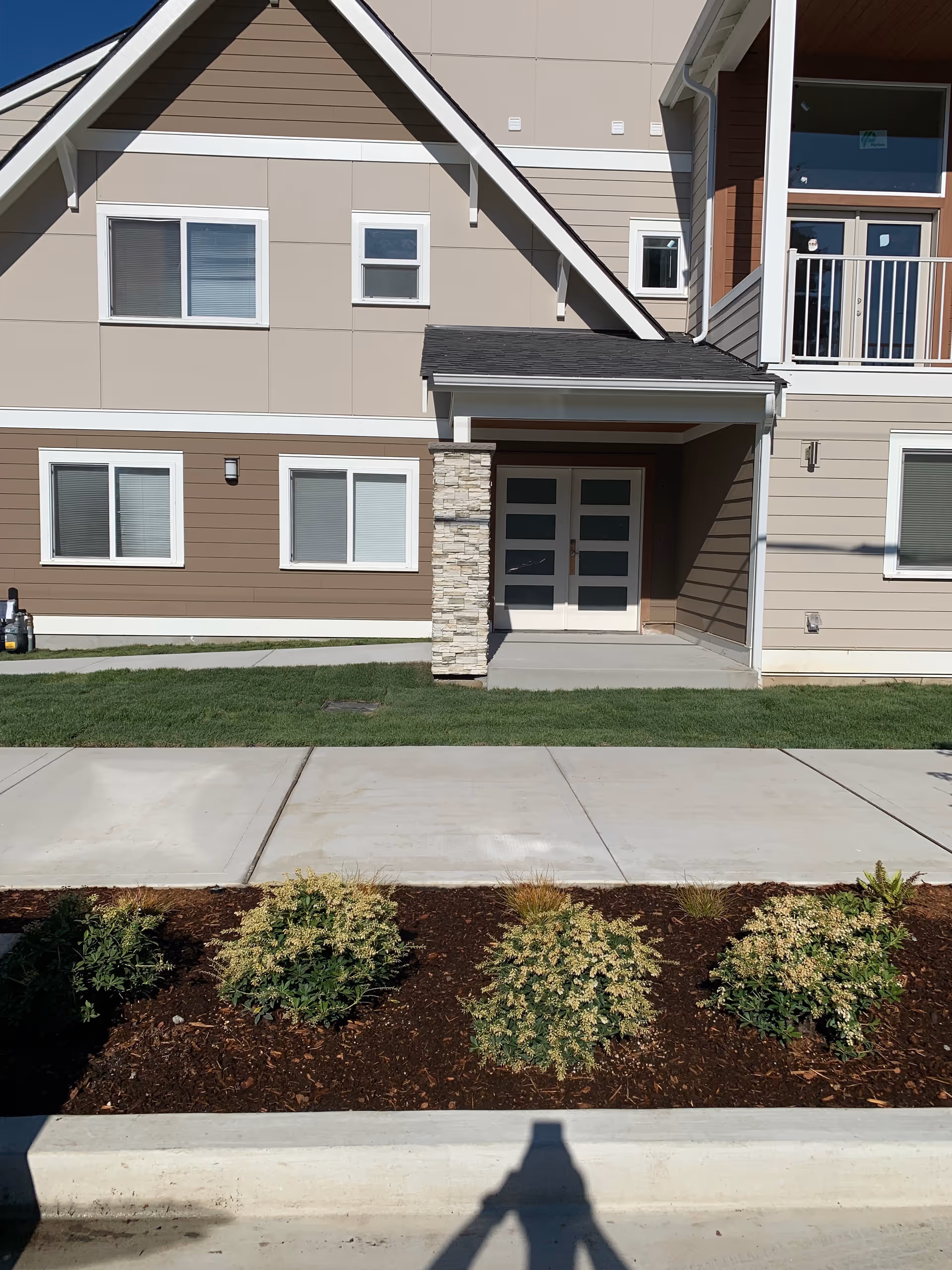 Exterior view of a beige apartment-style building with front entrance and landscaped walkway.
