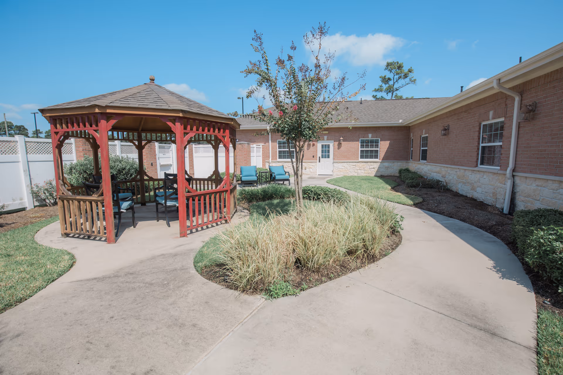 A courtyard with a red wooden gazebo, curved concrete walkways, landscaping, and a single-story brick building in the background.