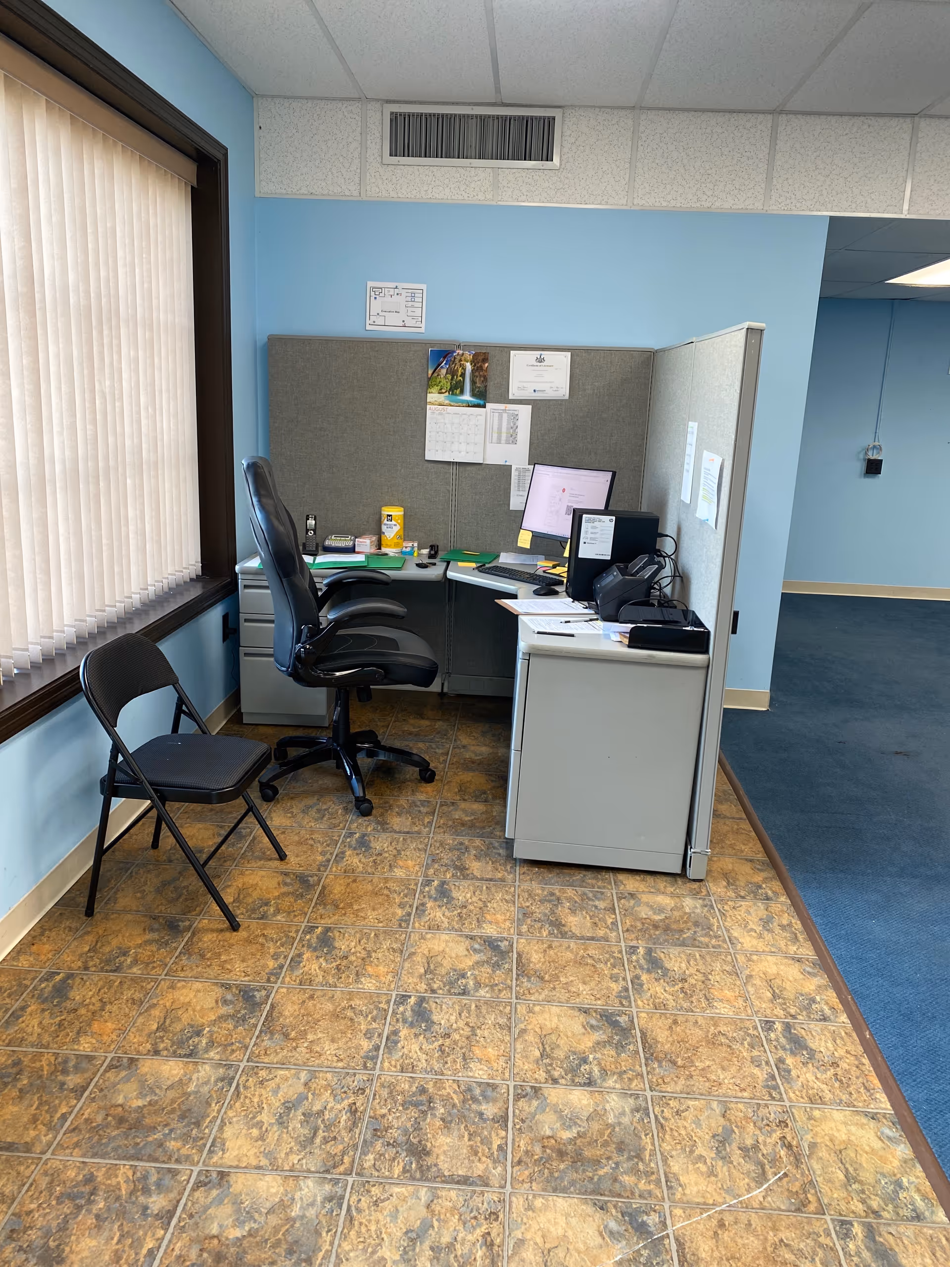 Office cubicle area with desk, computer, and chair inside a blue-walled facility.